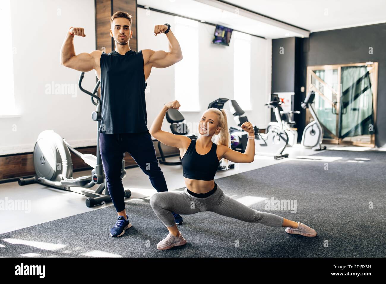 Ritratto di giovane coppia insieme in abbigliamento sportivo che mostra bicipiti in piedi in palestra, concetto sportivo, stile di vita sano Foto Stock