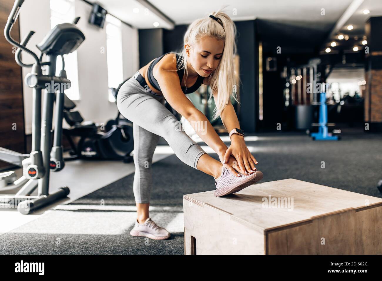 Giovane donna sportiva e attraente che si riscalda prima dell'allenamento e dell'ascolto alla musica con le cuffie in palestra Foto Stock