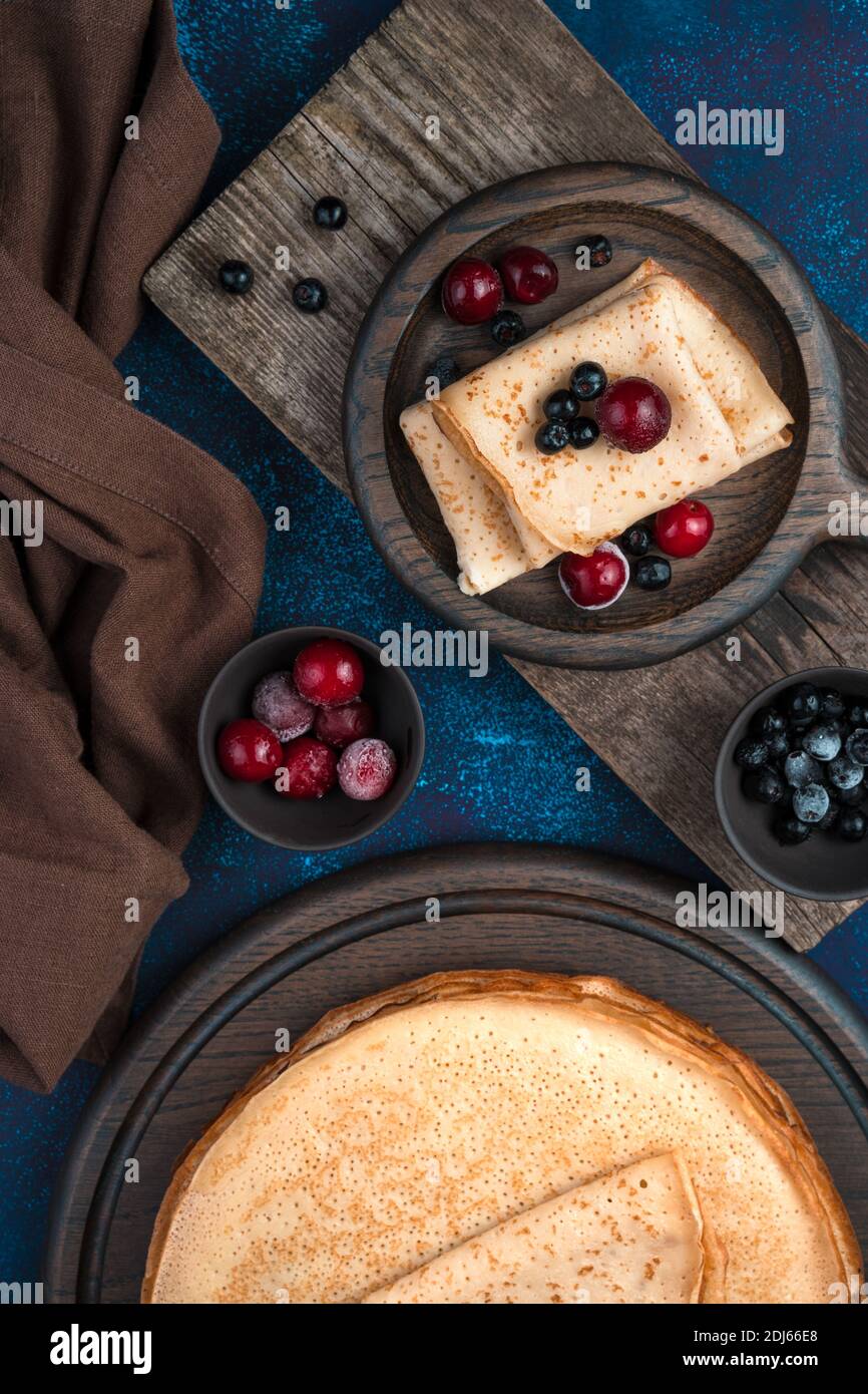 Pancake con frutti di bosco surgelati su un piatto di legno su sfondo blu scuro. Foto Stock