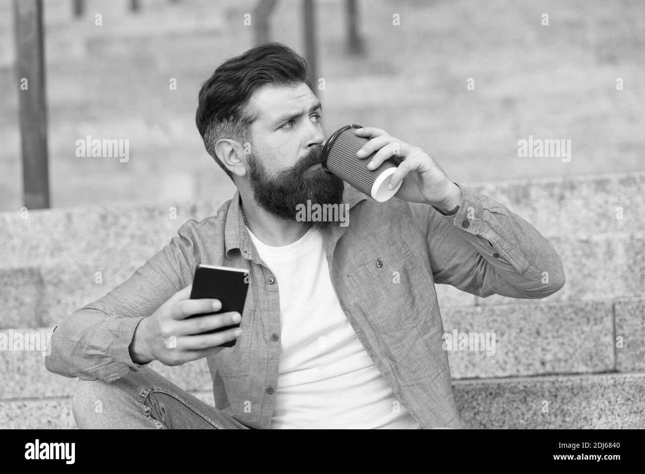 Bell'uomo con bearded rilassante telefono cellulare e caffè tazza. Vivere la vita online. Reti sociali. Comunicazione online di vita moderna. Ragazzo con smartphone di sfondo urbano. Tecnologia moderna. Foto Stock