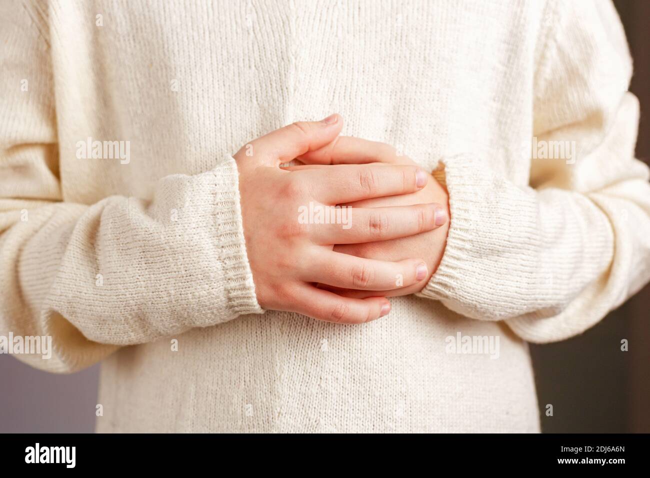 Primo piano delle mani di un bambino ripiegate sullo stomaco in un maglione lavorato a maglia leggera color champagne. Foto Stock