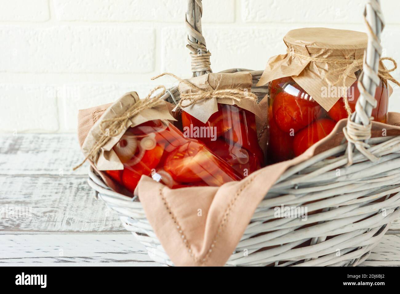 Pomodori fatti in casa conserve in vasi di vetro in bianco cesto di vimini su sfondo di legno. Foto Stock