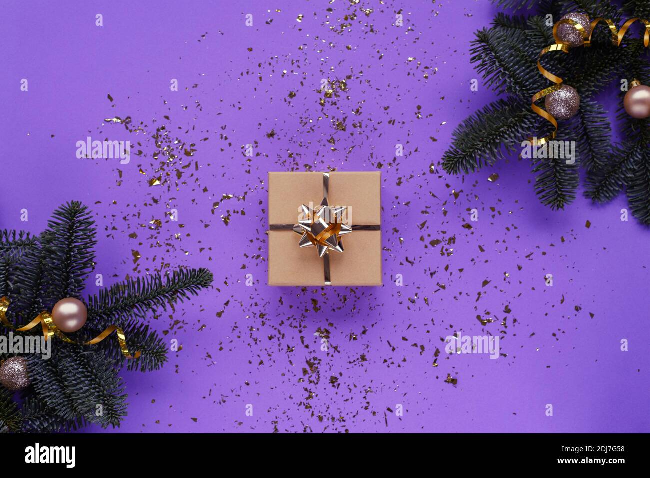 Rami di abete, regalo in scatola e baubles su sfondo viola con confetti. Concetto di Natale. Vista dall'alto, disposizione piatta. Foto Stock