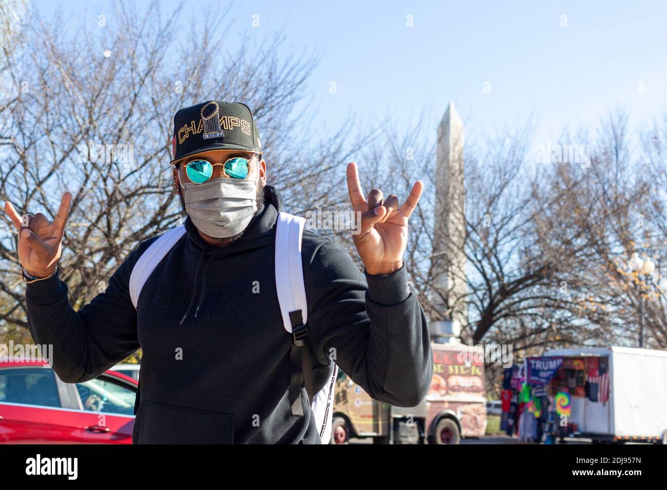 Washington DC, USA 11-29-2020: Un giovane uomo ispanico che indossa cappello da baseball, occhiali da sole polarizzati e maschera facciale a causa di COVID-19 è in posa con r Foto Stock