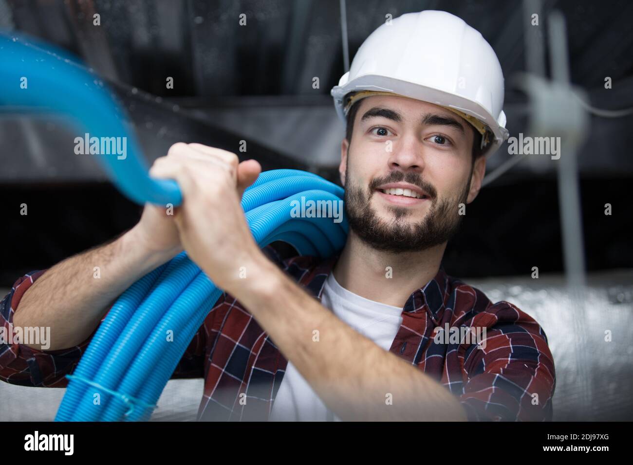 appaltatore maschio che installa il tubo blu nello spazio del tetto Foto Stock