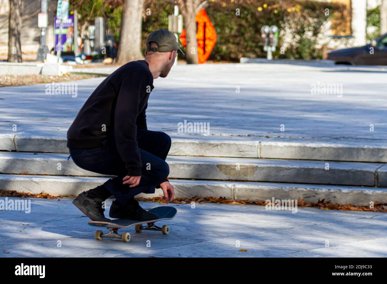 Un giovane caucasico indossa cappello, pantaloni in tela e sneakers sta sbattendo sul suo skateboard proprio prima di saltare in aria sopra le scale Foto Stock