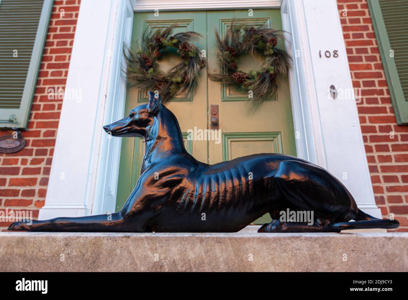 Frederick, MD, USA 12-02-2020: Un modello decorativo di cane nero lucido messo di fronte alla porta d'ingresso in legno di uno storico edificio in mattoni nella città vecchia. T Foto Stock