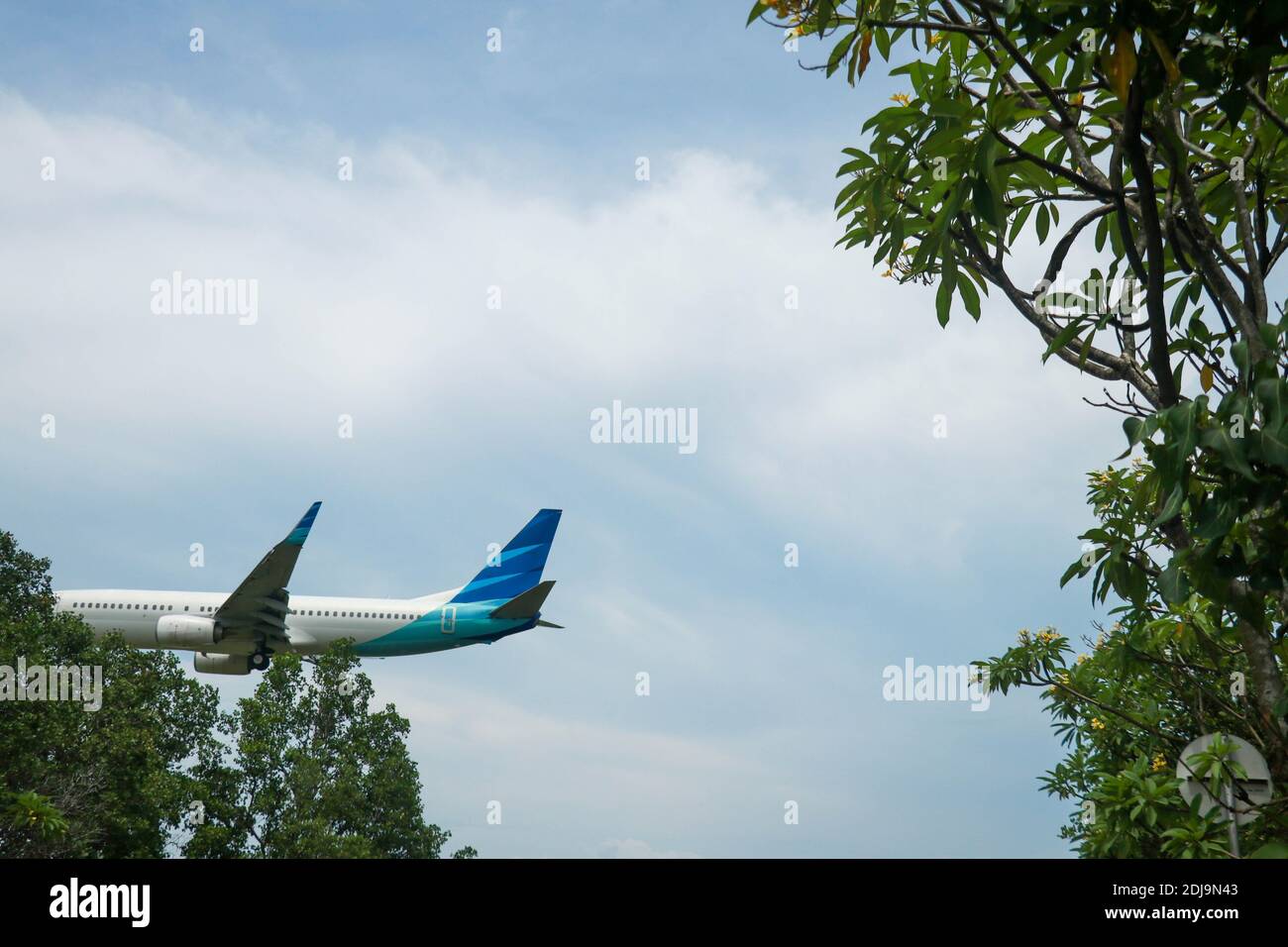 L'aereo parte dall'aeroporto internazionale con cielo blu e nuvoloso a Bali, Indonesia. Il velivolo su breve approccio finale per l'atterraggio a Ngurah Foto Stock