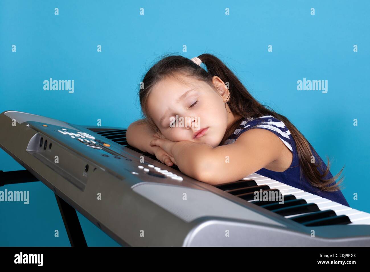 primo piano ritratto di una ragazza addormentata sulle chiavi di un sintetizzatore elettronico, stanco alla scuola di musica, isolato su sfondo blu Foto Stock