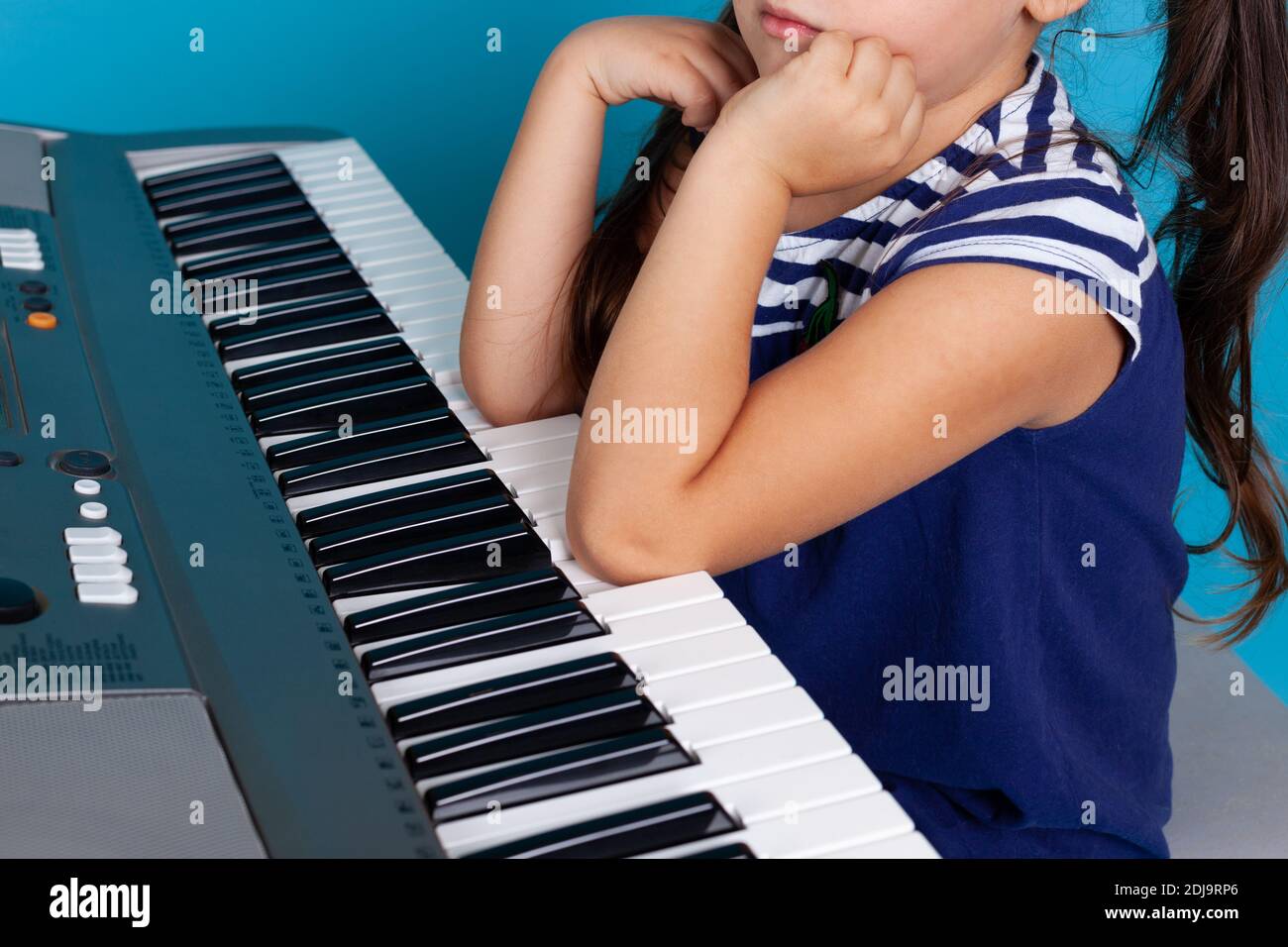 primo piano dei gomiti di un bambino premendo o suonando musica sui tasti del pianoforte, opzioni limitate, isolati su uno sfondo blu Foto Stock