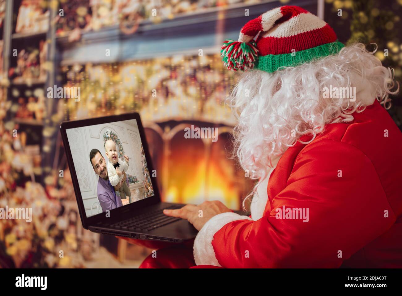 Babbo Natale sta guardando il portatile. Un uomo in un vestito di Natale al computer sullo sfondo delle luci di Capodanno. Il moderno mago. Natale h Foto Stock