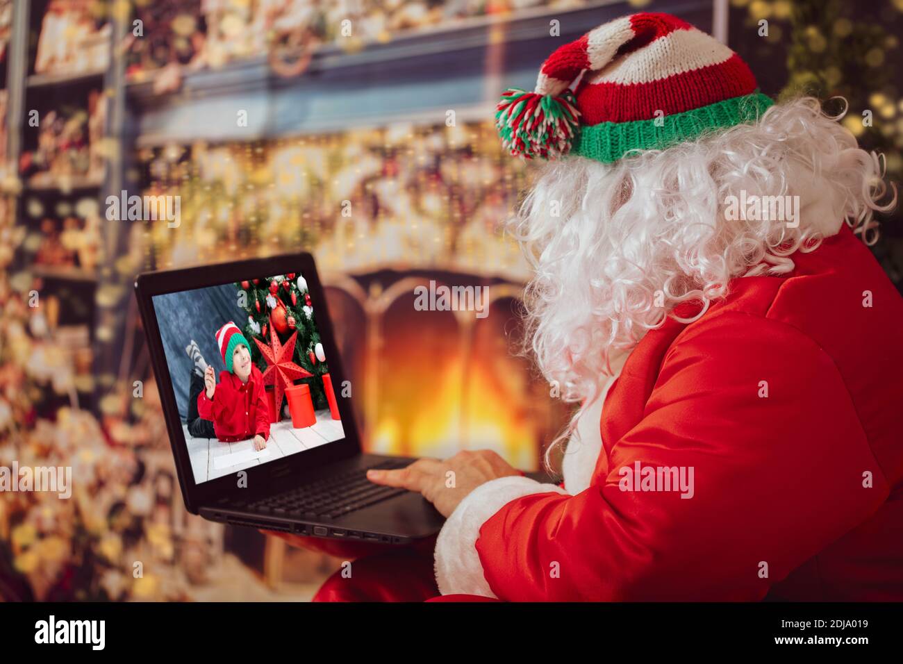 Babbo Natale sta guardando il portatile. Un uomo in un vestito di Natale al computer sullo sfondo delle luci di Capodanno. Il moderno mago. Natale h Foto Stock