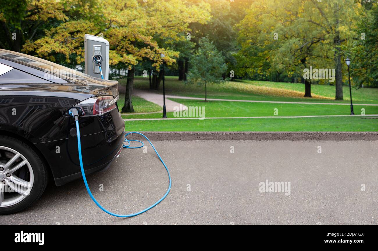 Auto elettrica con una stazione di ricarica sullo sfondo di parco cittadino Foto Stock