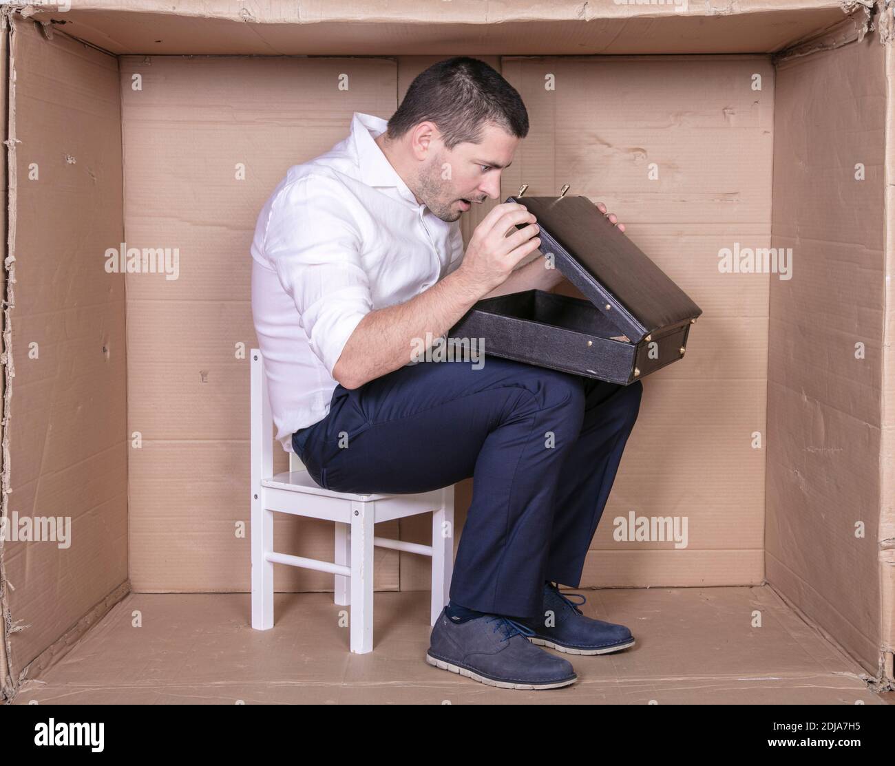 uomo d'affari con una valigetta si siede in una scatola di cartone stretta imitare un ufficio Foto Stock