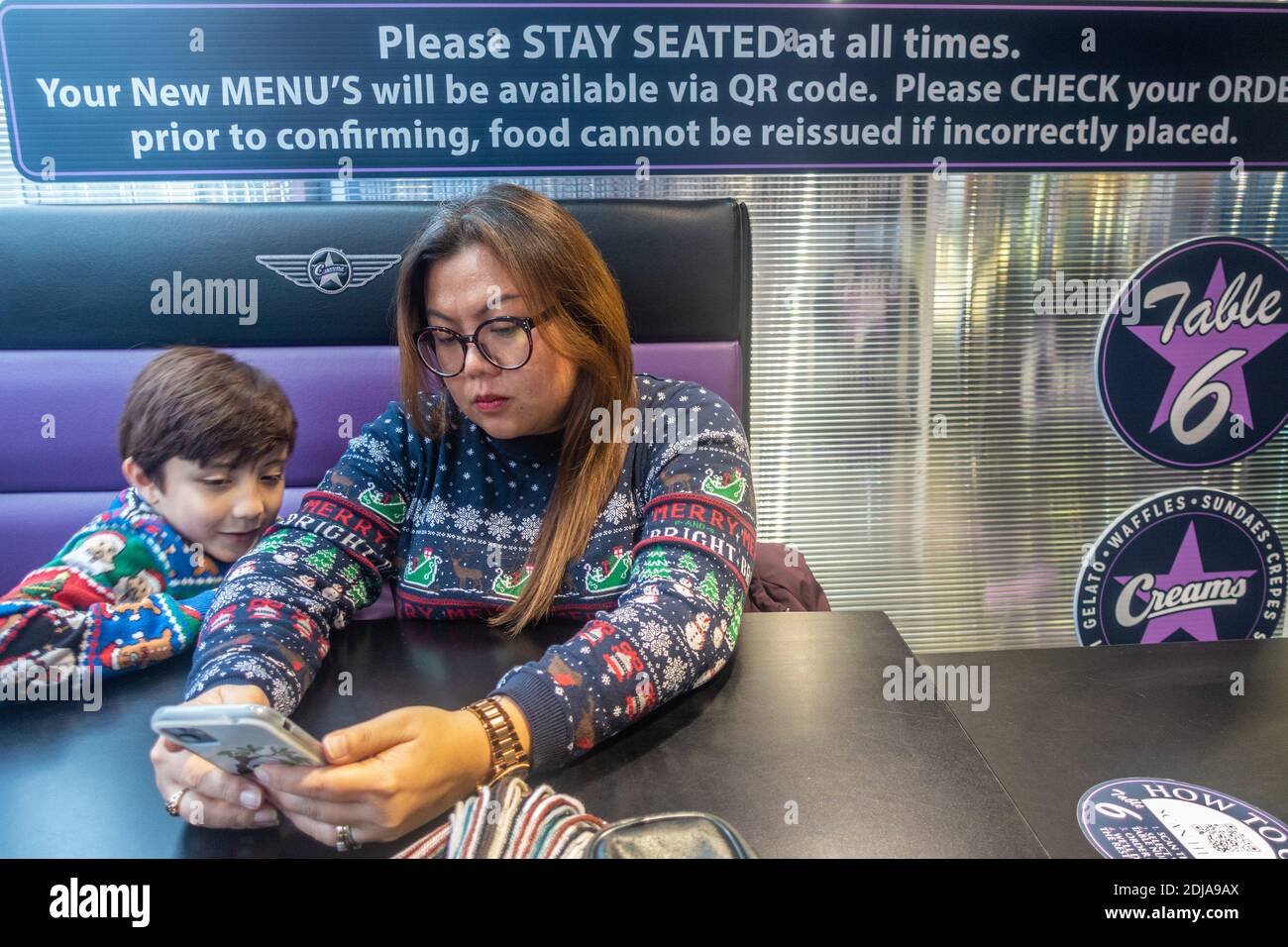 Una madre e un figlio ordinano il cibo in un bar utilizzando un'app su uno smartphone. Sopra di loro, le istruzioni spiegano come ordinare. Le istruzioni sono dovute al coronavirus Foto Stock