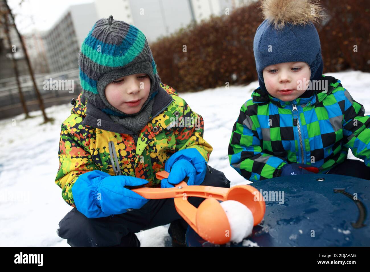 Fratelli che giocano con un produttore di palla di neve al parco giochi Foto Stock