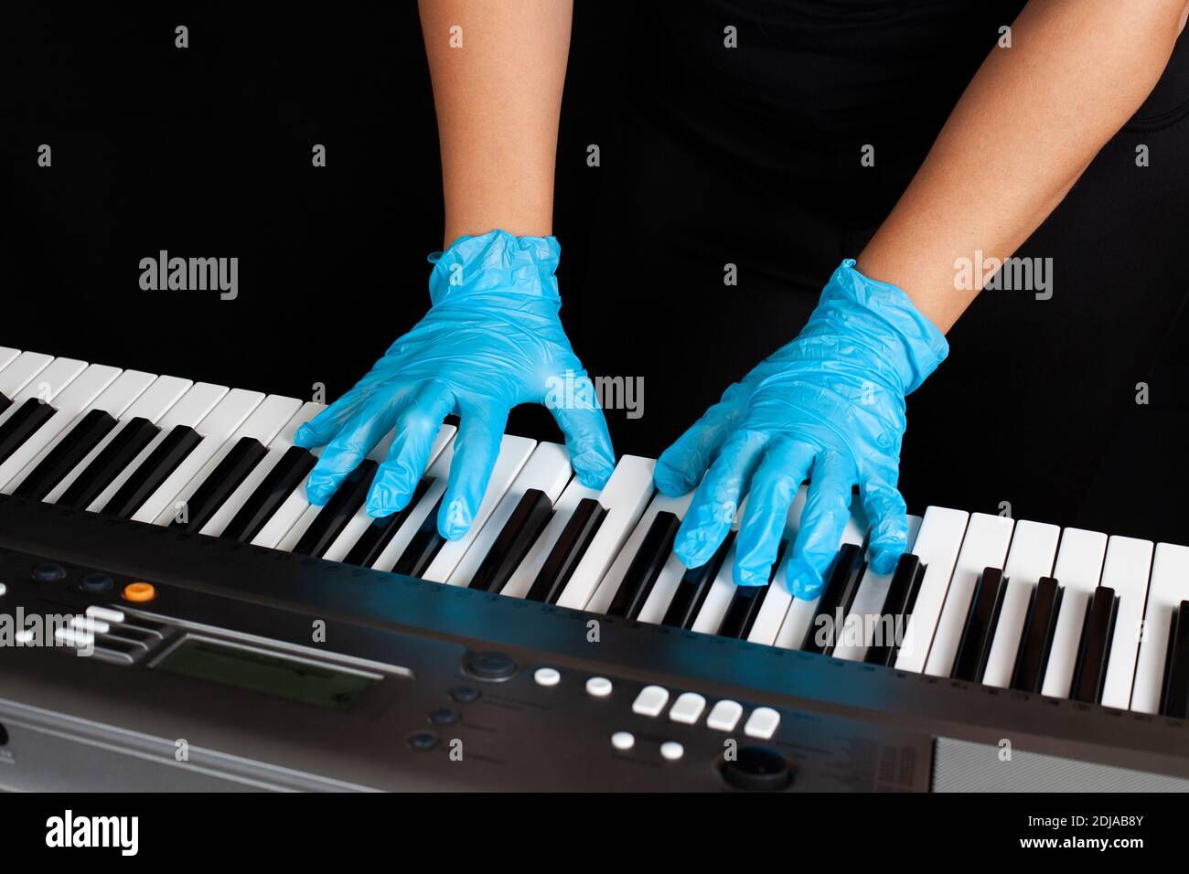 mani in guanti protettivi in gomma che suonano il pianoforte, protezione dai batteri del coronavirus ai concerti, su sfondo nero Foto Stock