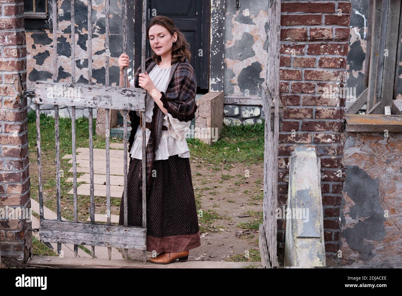 Una giovane donna in abiti vintage canta una canzone vicino al vecchio cancello. Abito retrò in stile Halloween 18-19 ° secolo Foto Stock
