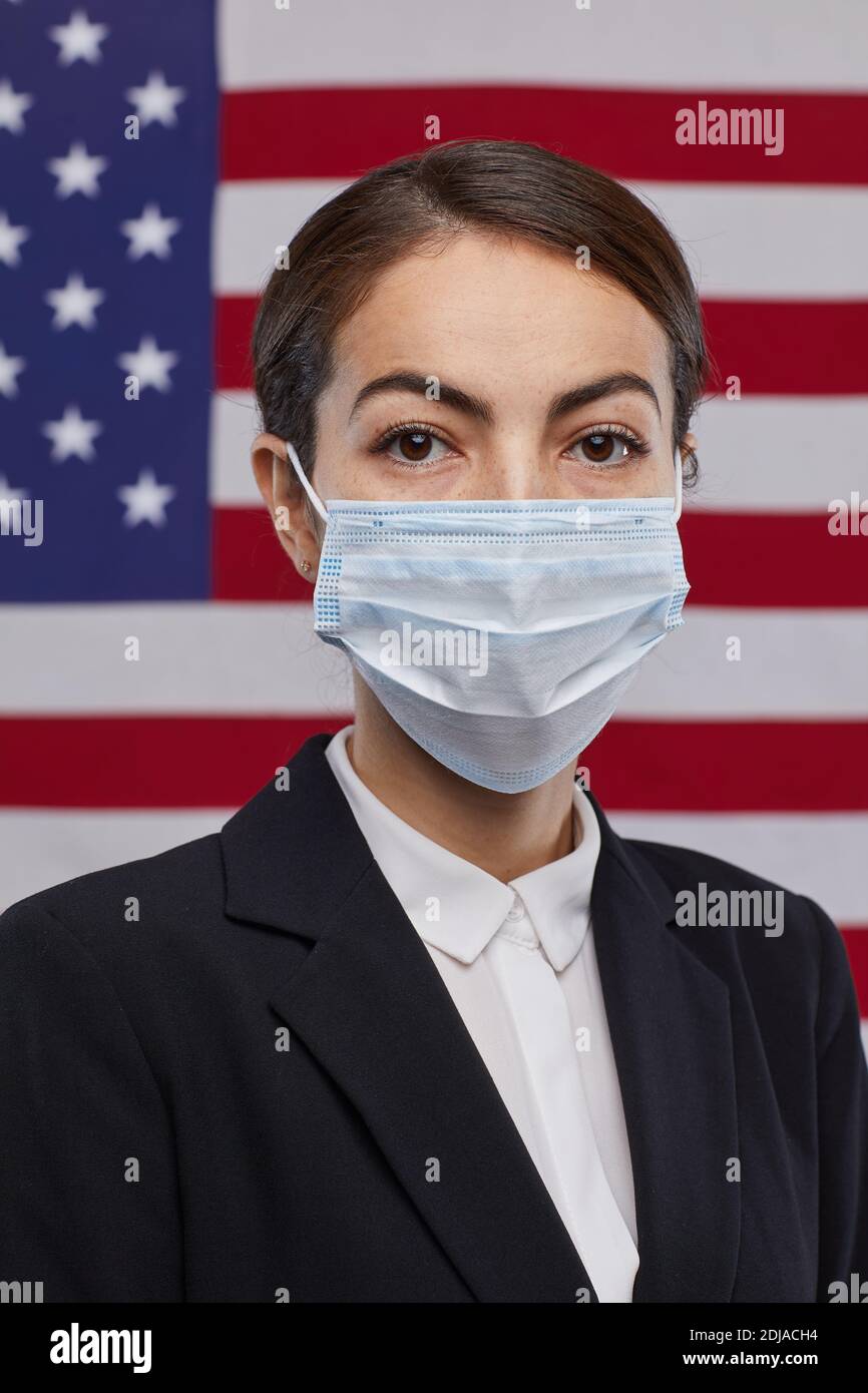 Ritratto verticale di donna uomo politico indossando maschera e guardando Fotocamera mentre si sta in piedi contro lo sfondo della bandiera degli Stati Uniti Foto Stock
