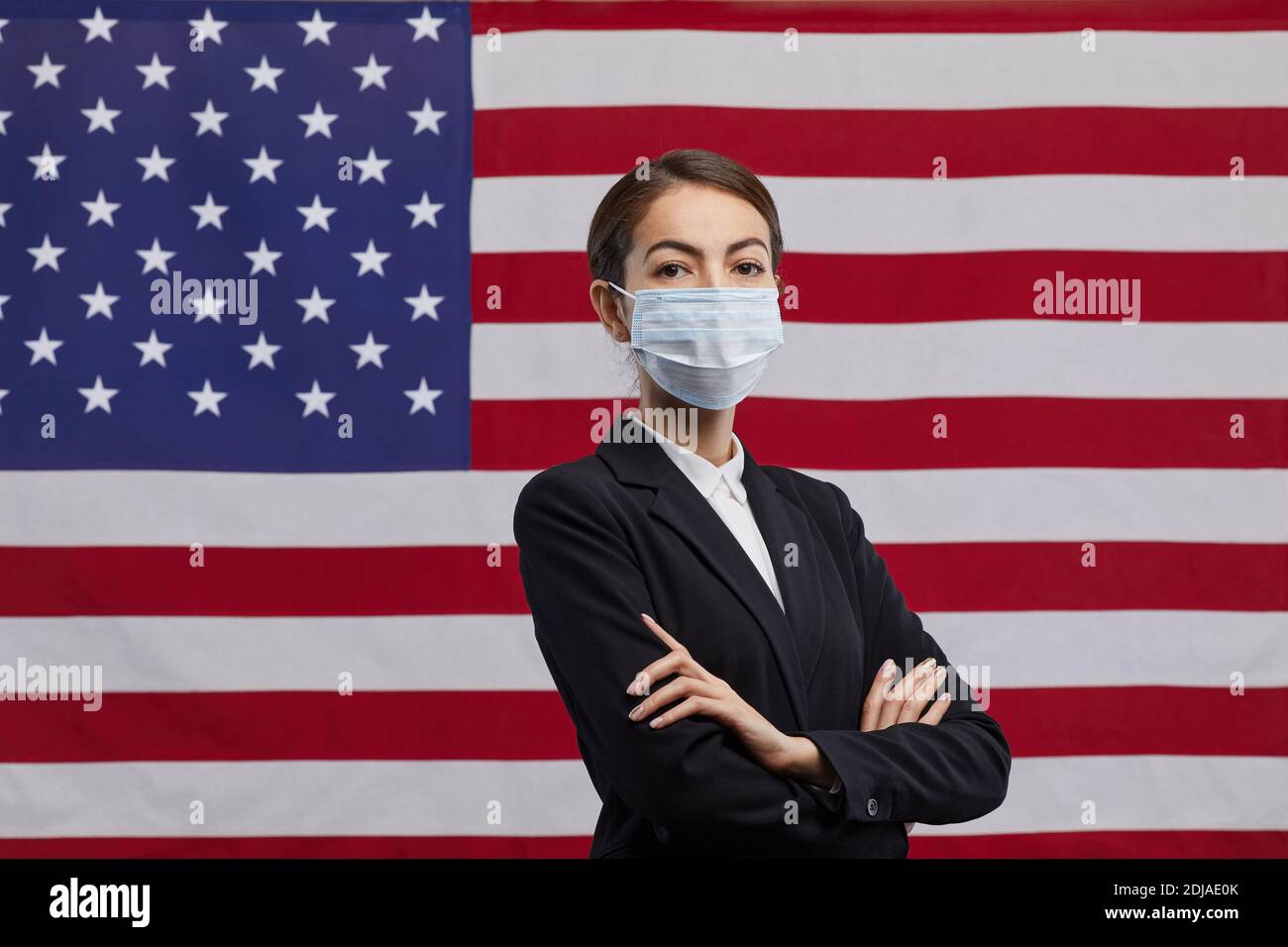 Vita in su ritratto di donna sicura uomo politico indossare maschera e guardando la fotocamera in piedi con le braccia incrociate contro lo sfondo bandiera USA, copia Foto Stock