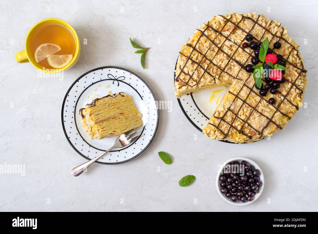 Torta alla vaniglia multistrato decorata con frutti di bosco, menta. Un pezzo di deliziosa torta su un piatto e una tazza di tè del mattino con limone. Vista dall'alto. Foto Stock