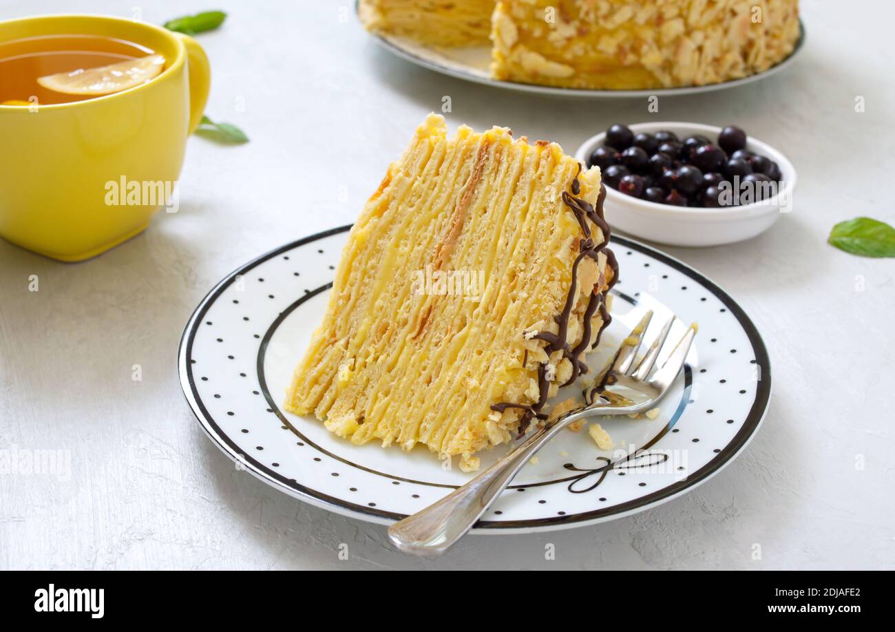 Un pezzo di torta alla vaniglia multistrato su un piatto e una tazza di tè del mattino con limone. Foto Stock