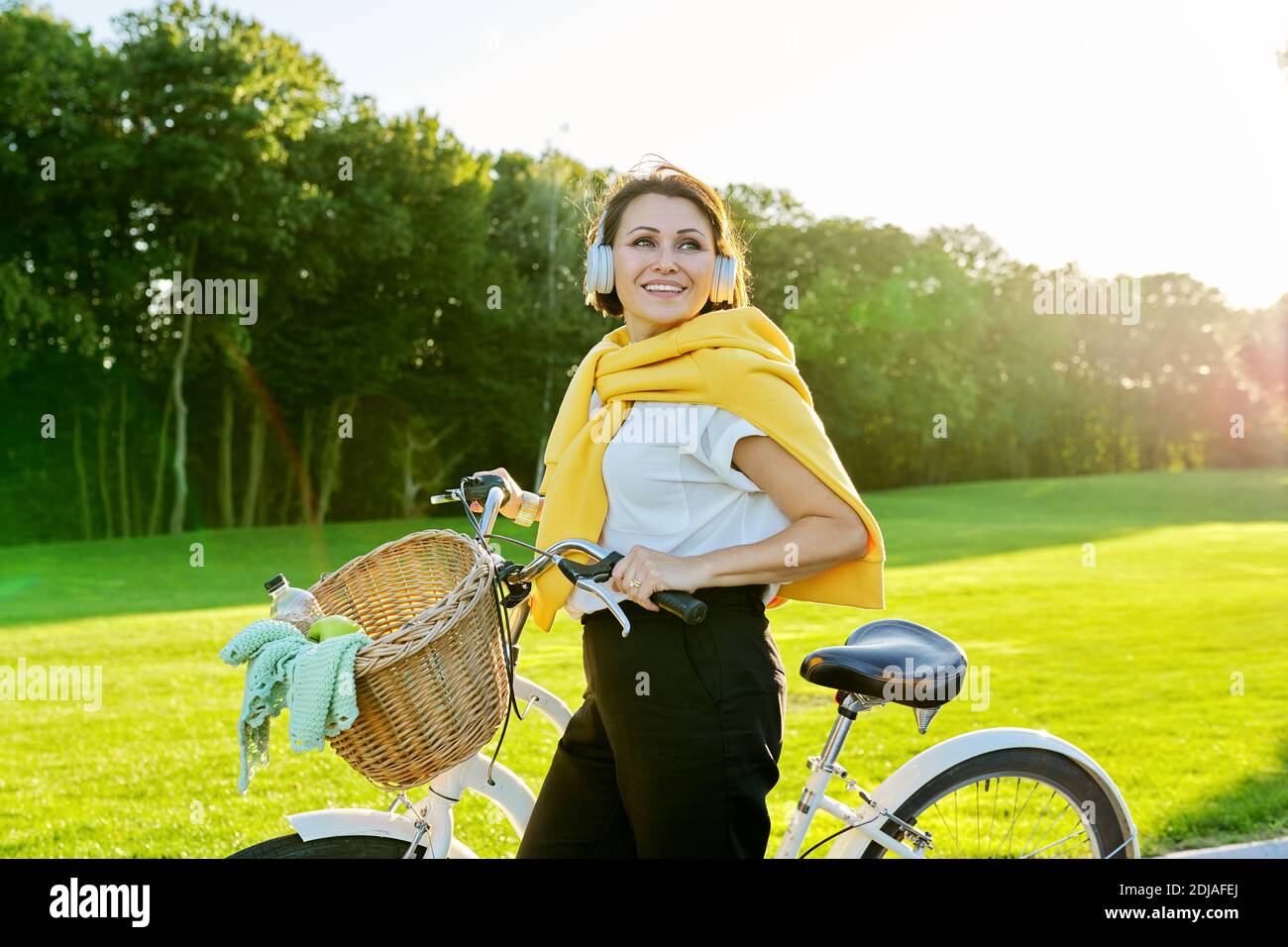 Bella donna di mezza età felice in cuffia con bicicletta nel parco Foto Stock
