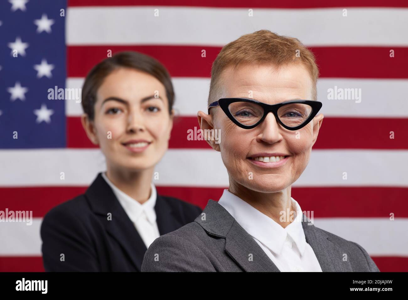 Primo piano ritratto di due politici fidati che guardano la fotocamera mentre si levano in piedi contro lo sfondo della bandiera degli Stati Uniti, copy space Foto Stock