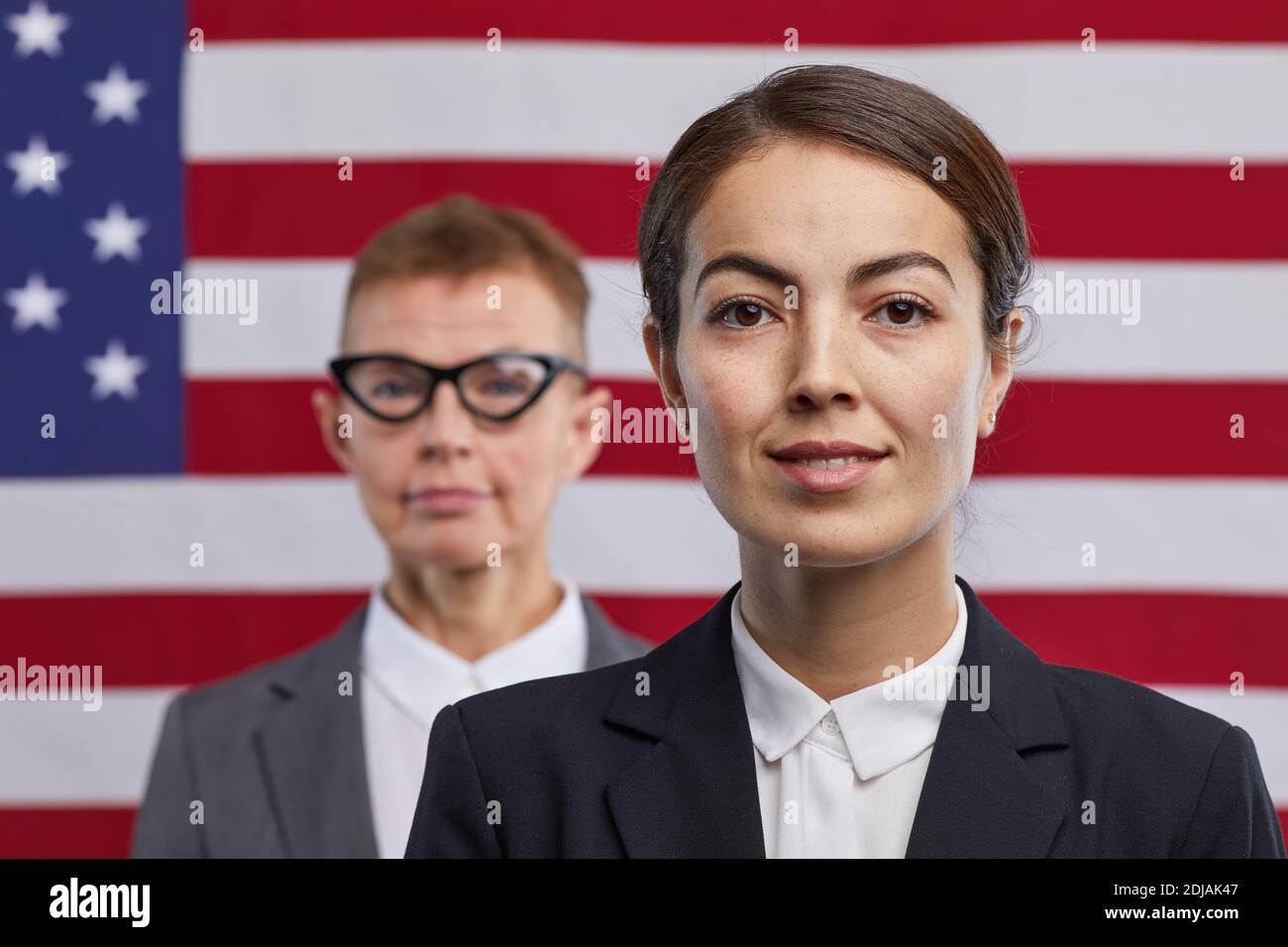 Primo piano ritratto di giovane donna politico guardando la macchina fotografica e sorridendo mentre si sta in piedi contro lo sfondo della bandiera degli Stati Uniti, copia spazio Foto Stock