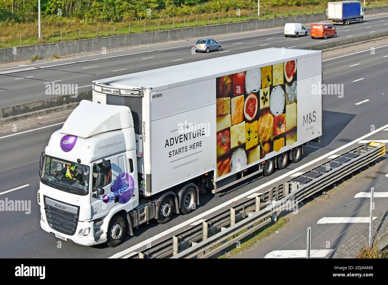 Vista laterale e anteriore camion e conducente con Consegna M&S da parte del settore alimentare al dettaglio rimorchio della catena di fornitura refrigerata Grafica pubblicitaria sull'autostrada del Regno Unito Foto Stock