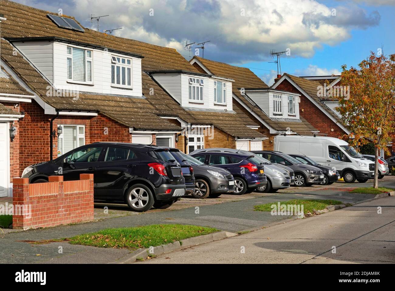 Strada residenziale scena parcheggio auto fuori strada e case con auto e furgone su giardini originali fronte prato ora in cemento Spazio per veicoli Essex Inghilterra UK Foto Stock