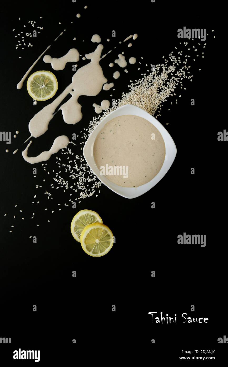 Salsa di tahini fatta in casa, semi di sesamo finiscono il limone su sfondo nero. Cibo vegetariano. Cibo sano. Opuscolo promozionale e poster. Disposizione piatta. Foto Stock