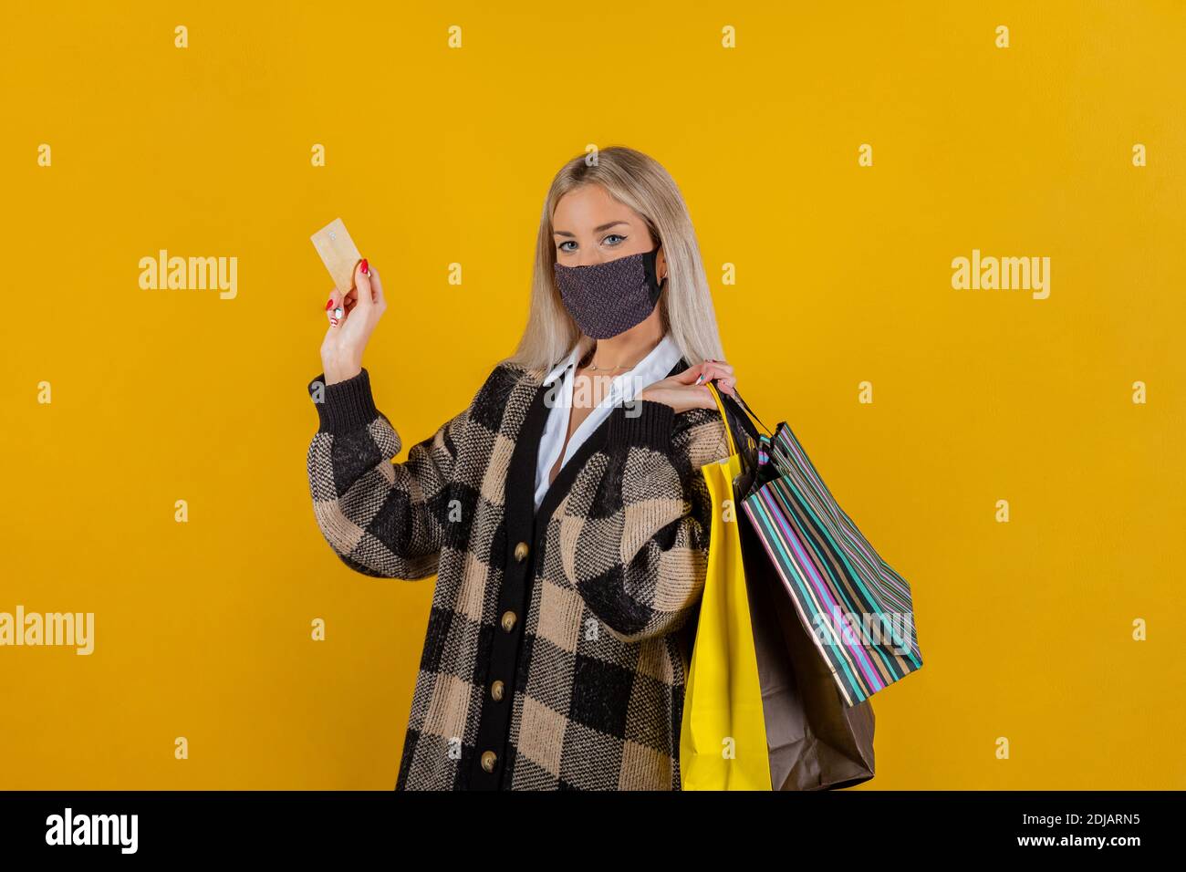 Donna alla moda che indossa una garza di sicurezza verde maschera per la prevenzione da coronavirus Covid19 pandemia, con borse e carta di credito in mano Foto Stock