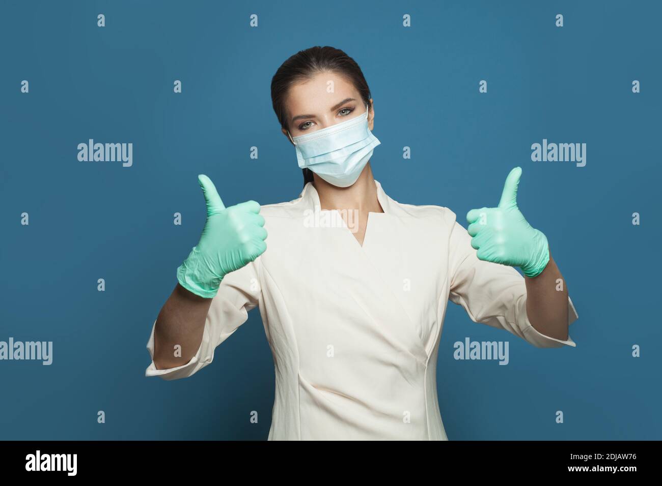 Buon medico che tiene il pollice su sfondo blu. Medicina, sicurezza, vaccinazione e protezione del virus covid-19 concetto Foto Stock