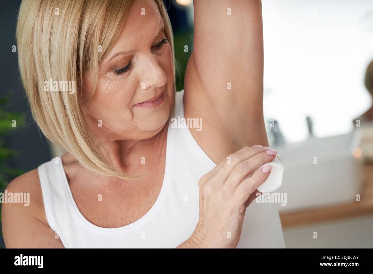 Donna anziana che usa il roll-on deo in bagno Foto Stock
