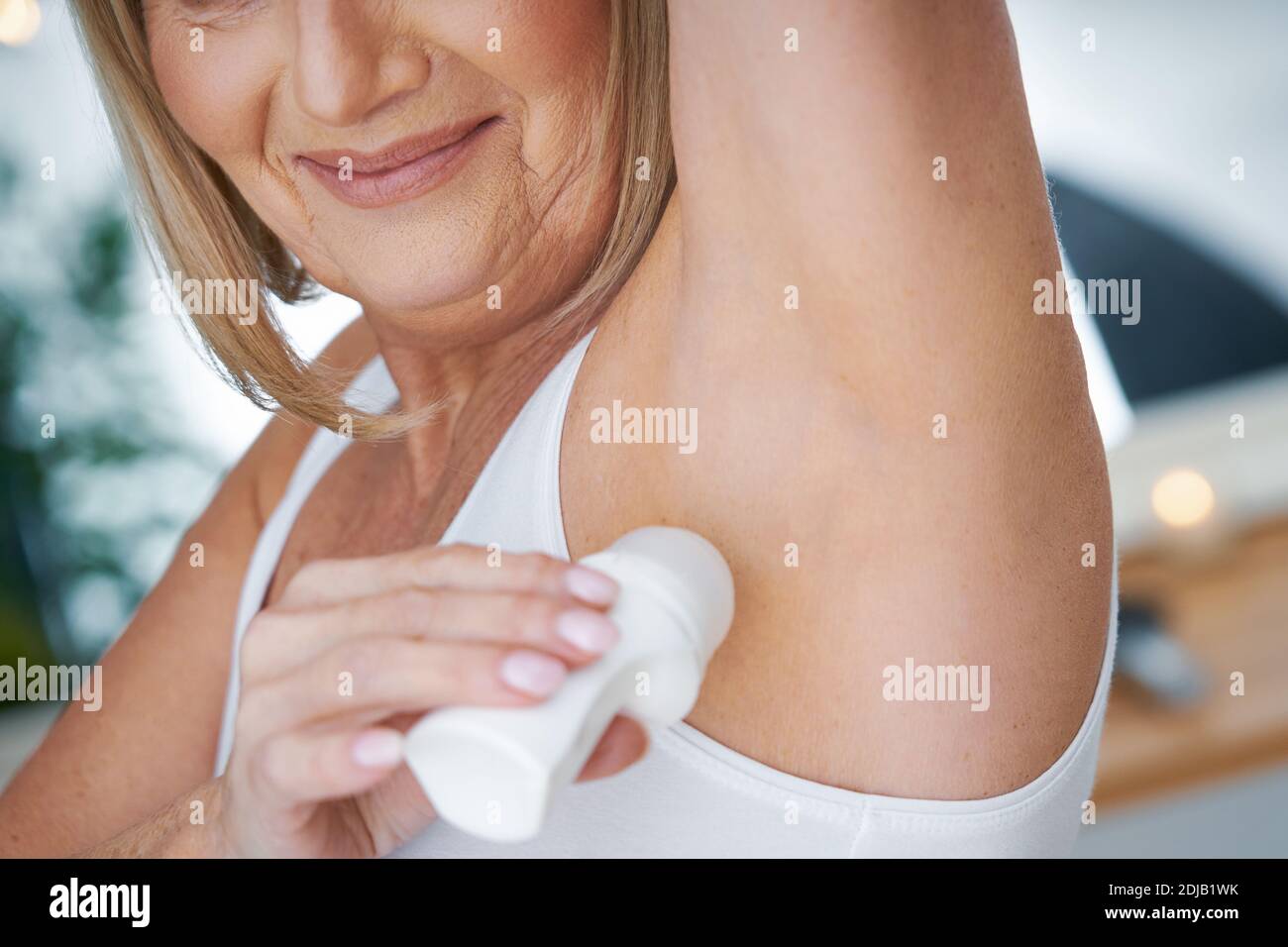 Donna anziana che usa il roll-on deo in bagno Foto Stock