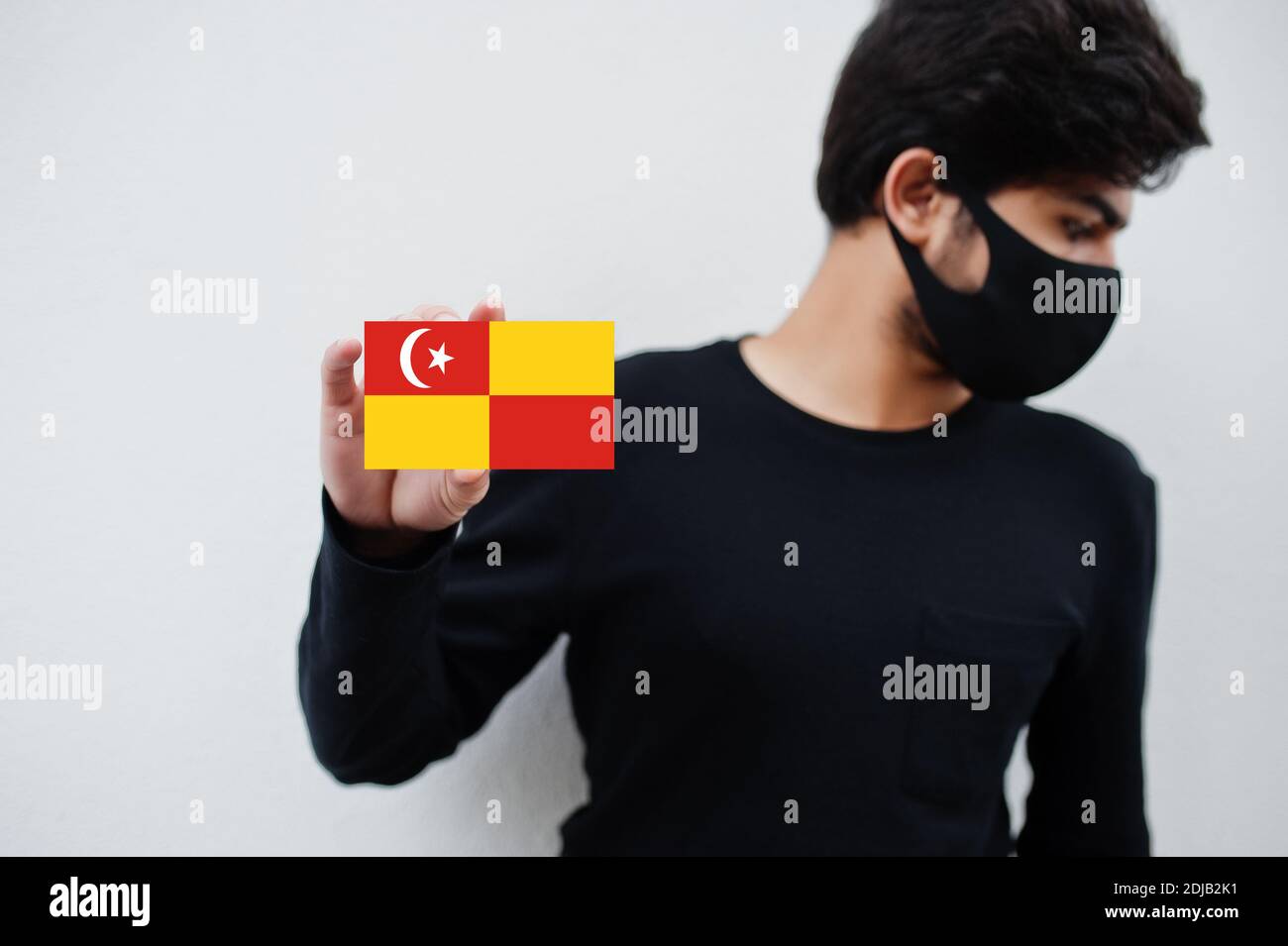 Uomo malese indossare tutto nero con maschera faccia tenere la bandiera Selangor in mano isolato su sfondo bianco. Stati e territori federali della Malaysia coronaviru Foto Stock