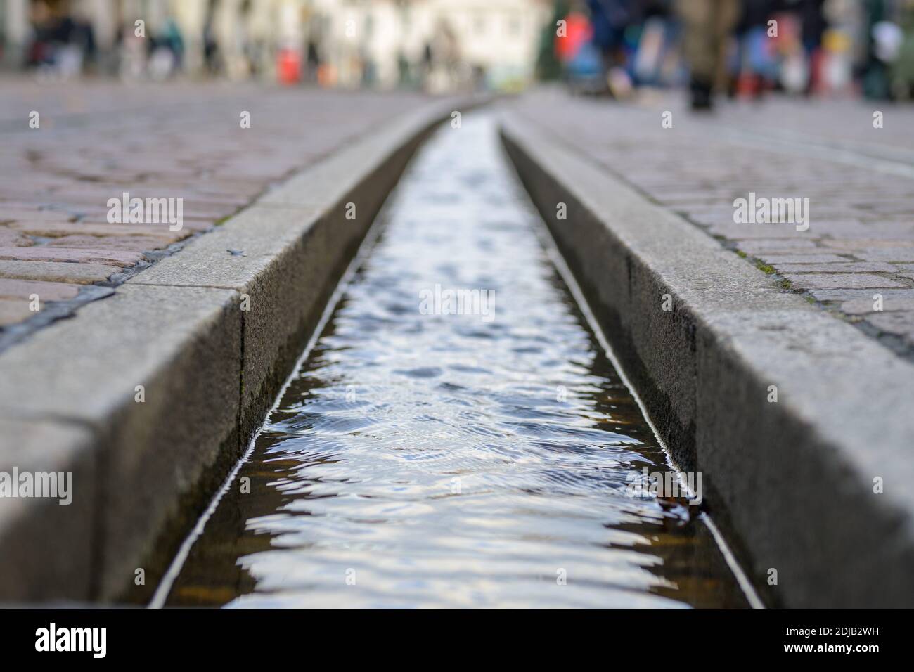 Il runnel d'acqua di Friburgo Bächle in primo piano e a fuoco selettivo al piano terra con i pedoni che camminano per la strada Foto Stock