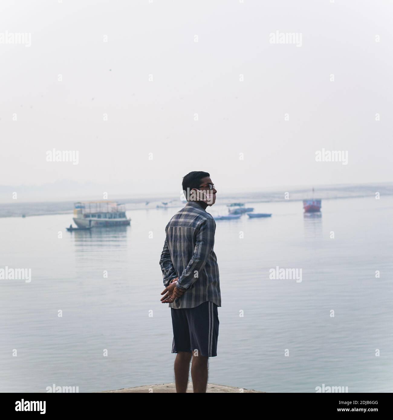 Un uomo in piedi sui ghat del fiume ganga nella città Santa di varanasi, pradesh più in india. Indossa una maschera, ma non in modo appropriato Foto Stock