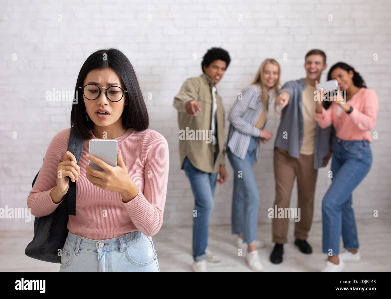 Umiliazione, educazione e bullismo. Triste asian giovane femmina in occhiali guarda il telefono Foto Stock