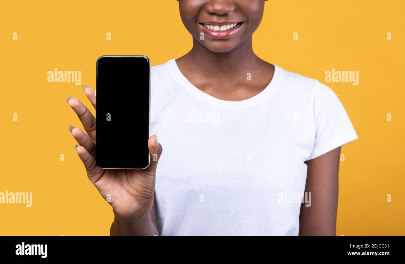 Donna nera irriconoscibile che mostra lo schermo del telefono cellulare su sfondo giallo Foto Stock