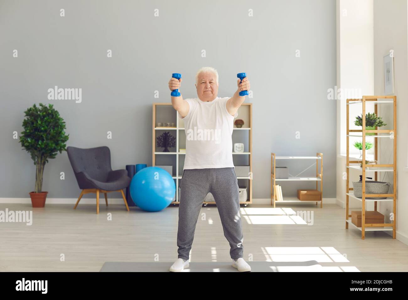 Uomo anziano determinato che si esercita con i manubri durante uno sport di routine allenati a casa Foto Stock