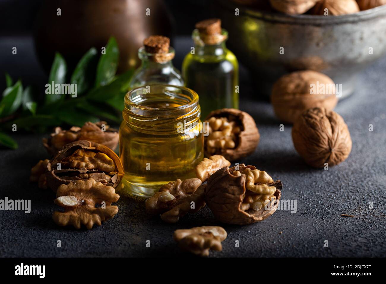 Olio di noce cosmetico e terapeutico su fondo di legno. Olio di noce in bottiglia e noci su fondo scuro. Foto Stock