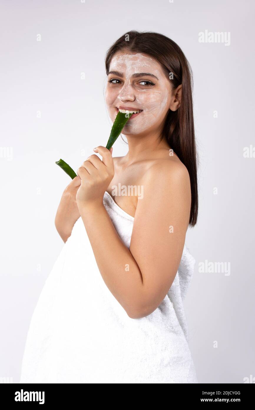 Una ragazza brunette con maschera facciale sul viso tiene una foglia di  aloe rotta nei denti. Foto su sfondo bianco Foto stock - Alamy