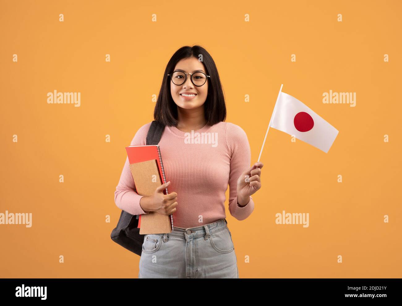 Studio linguistico e scambio di studenti. Sorriante giovane donna asiatica che tiene bandiera giapponese Foto Stock