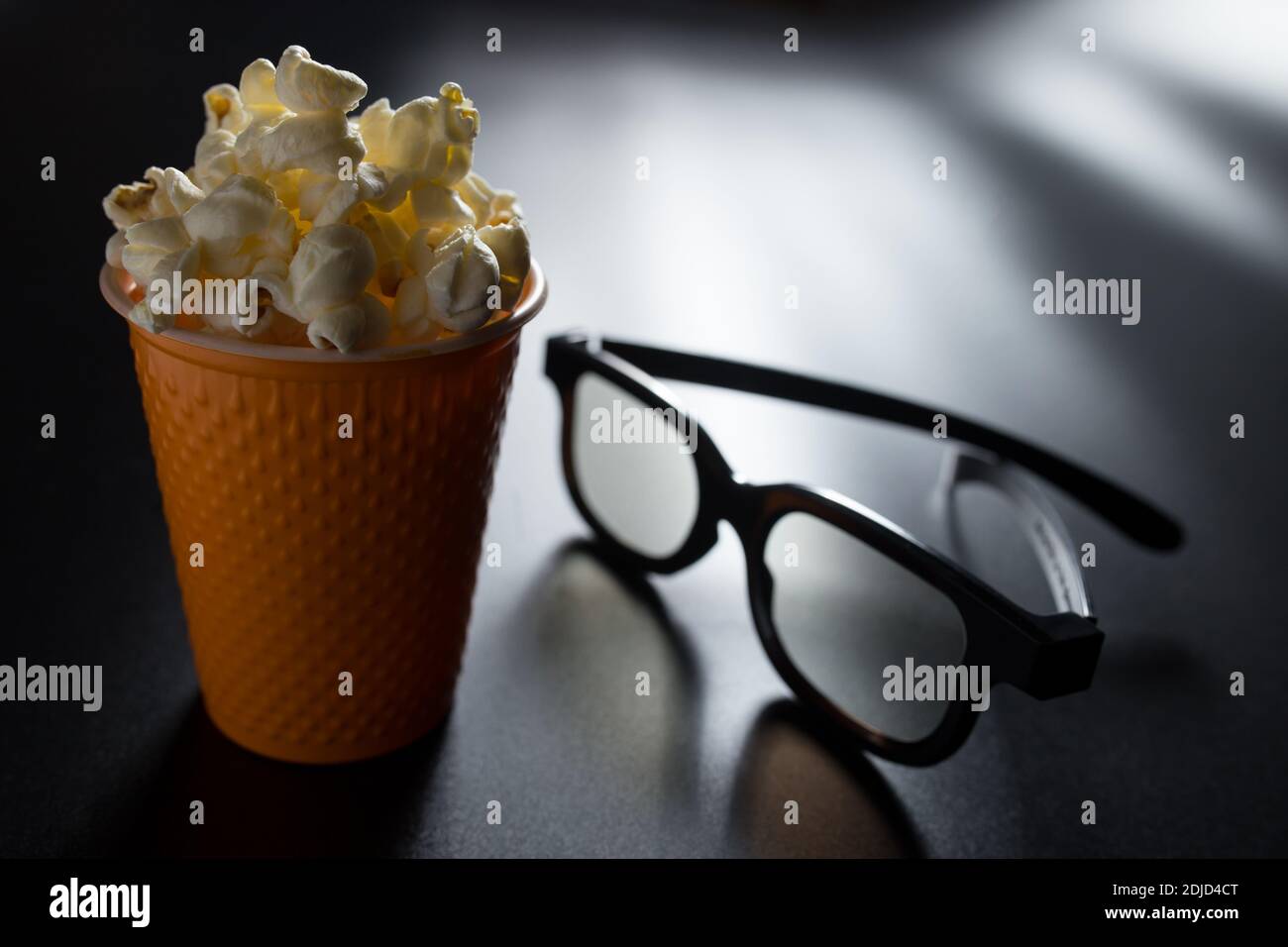 Guardare un film in 3D a casa con popcorn. Secchio di popcorn e bicchieri 3D su sfondo nero. Foto Stock