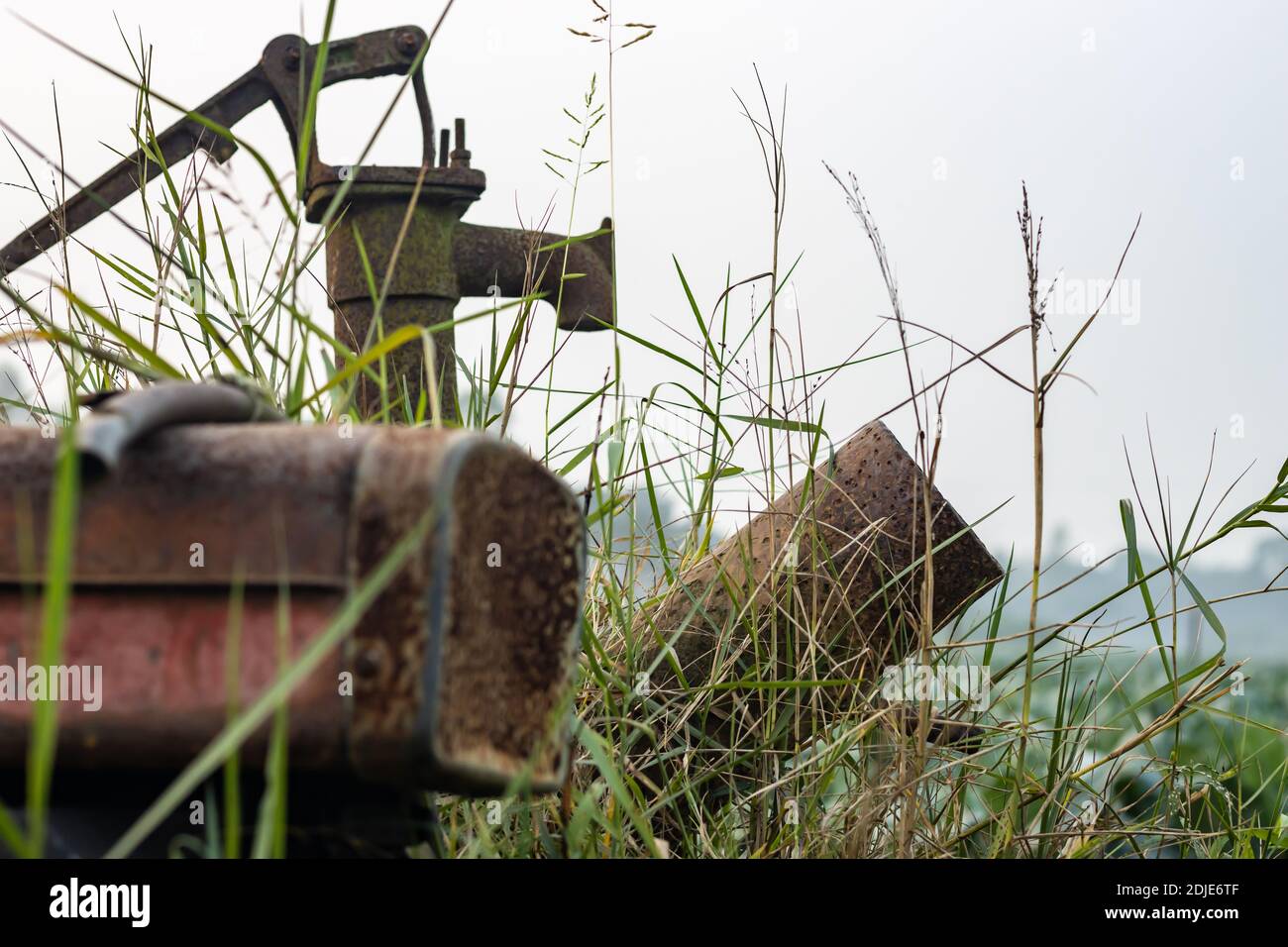 Una pompa inutile di acqua arrugginita nel campo agricolo all'interno le erbe selvatiche Foto Stock