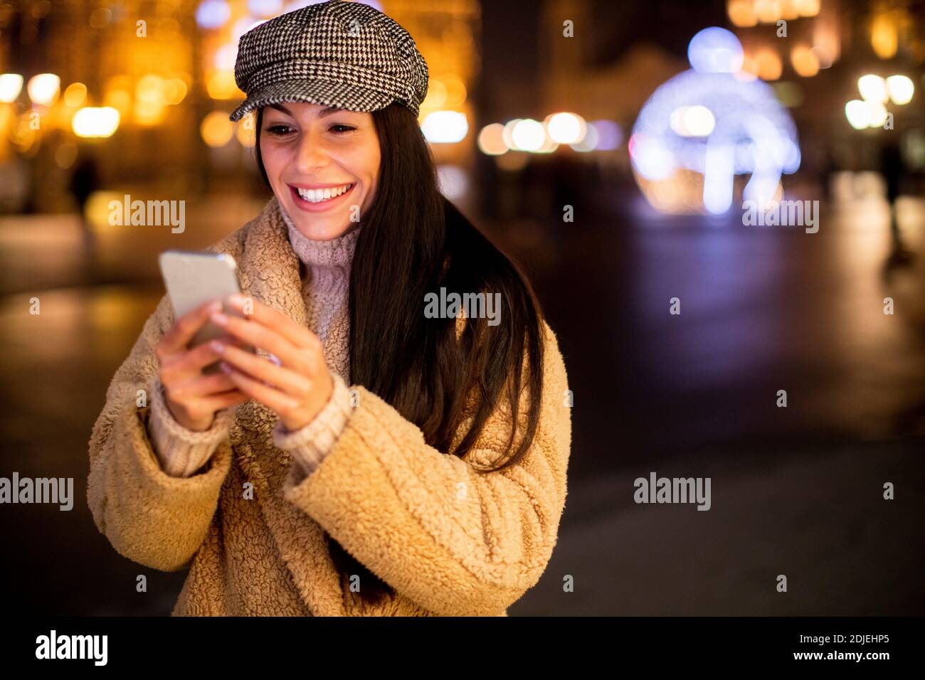 Bella giovane donna che usa il suo cellulare per strada A Natale Foto Stock