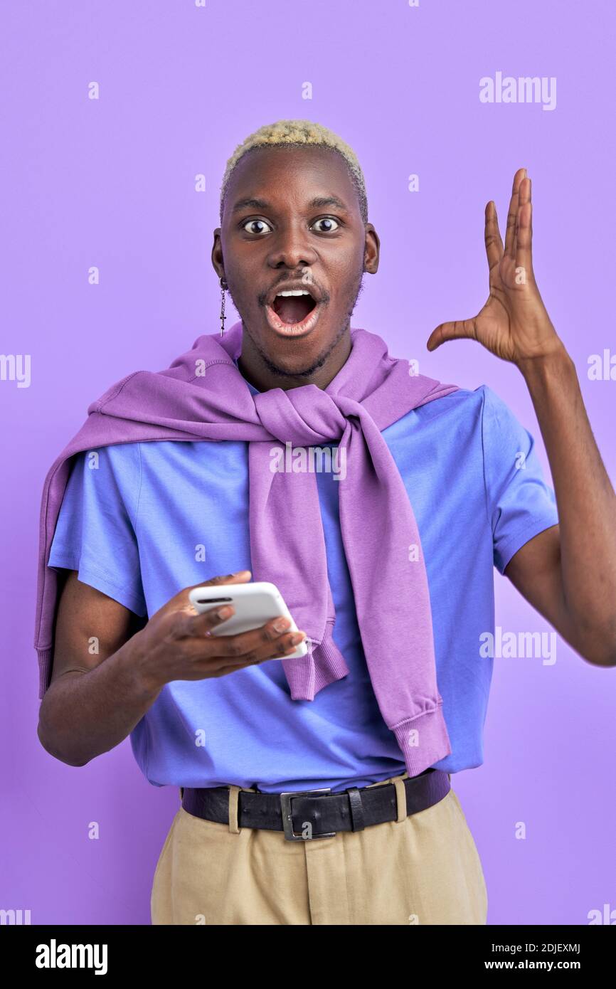 l'uomo nero è in shock da notizie, mentre chattando con l'amico su smartphone, è sorpreso, mostra emozioni, gesturing con le mani. isolato su viola ba Foto Stock