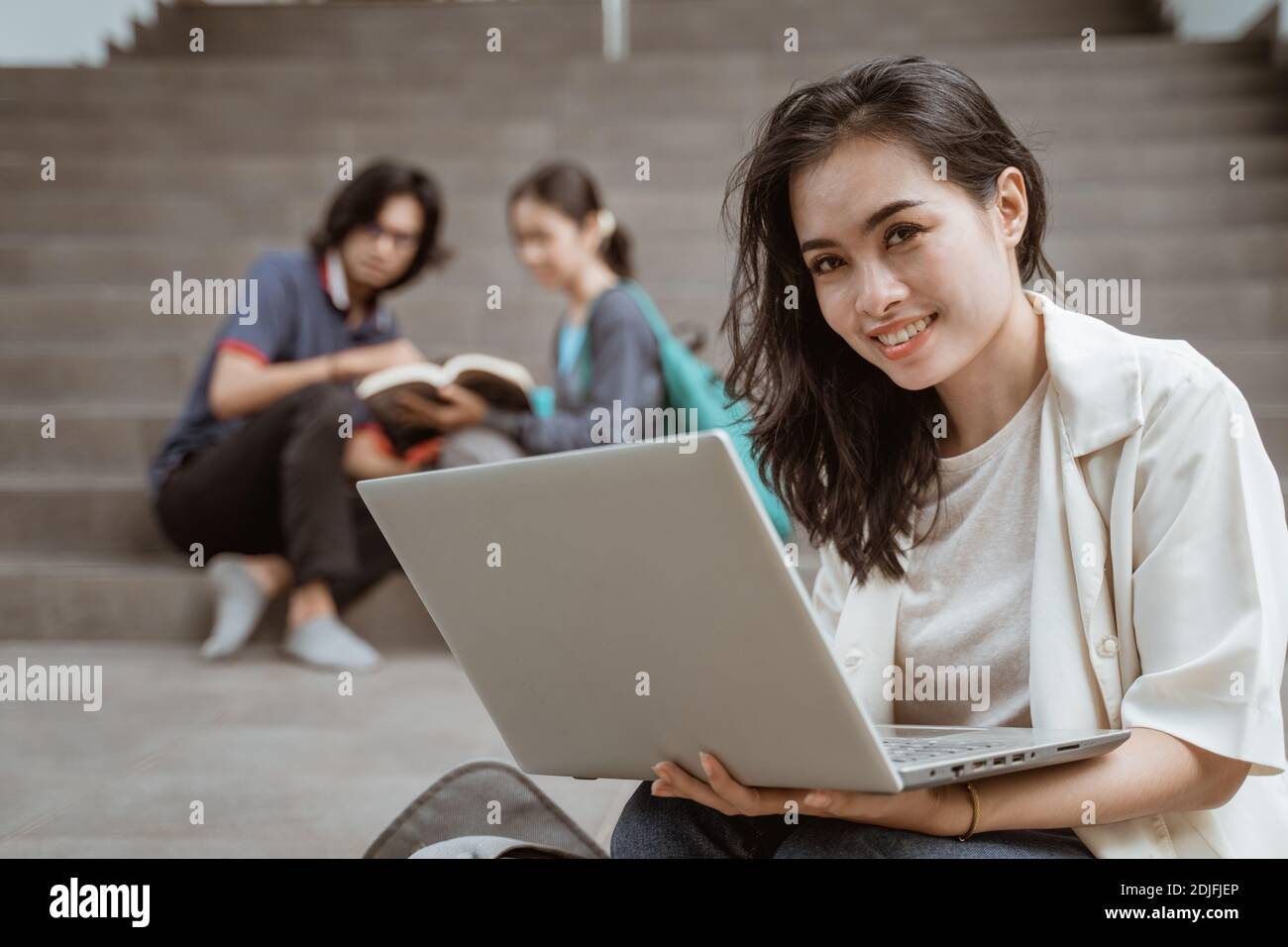 Ritratto felice studenti che tengono computer portatili con amici in background Foto Stock